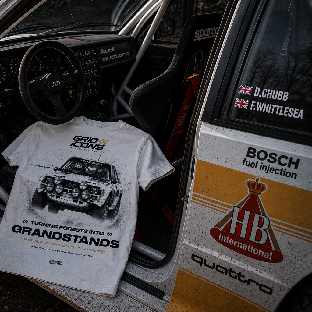 A white graphic t-shirt featuring a rally car print and the text 'GRID ICONS GRANDSTANDS' is draped over the open door of a vintage rally car. The car door is decorated with sponsor decals including Bosch, HB International, and Quattro, and the background shows a blurred forest.